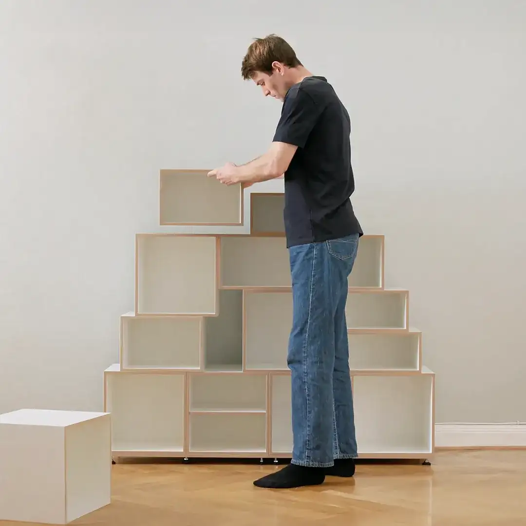 Ein Mann in Jeans und dunklem T-Shirt hält ein stocubo 2:3-Modul und baut damit ein versetztes, modulares Regalsystem zusammen.