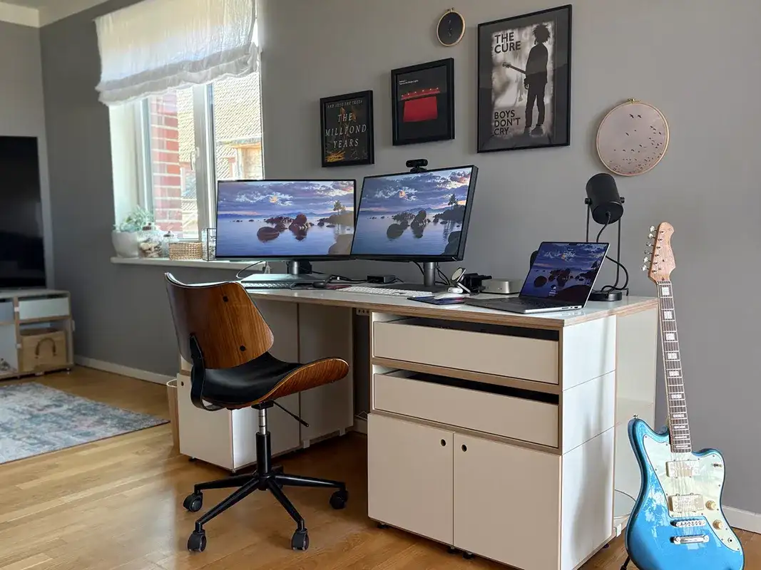 Kundenbilder, a modular desk in a home office setup with three computers, a blue guitarre standing on the floor on the right side and framed music posters above it.